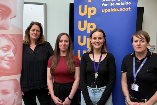 Four women standing in front of promotional banners at the launch of the Upside service in Moray. One banner displays the Upside logo and slogan "A helping hand for life outside" with the website upside.scot