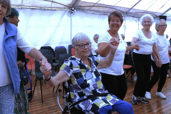 A woman seated in a wheelchair joins a chain of woman all linking hands.