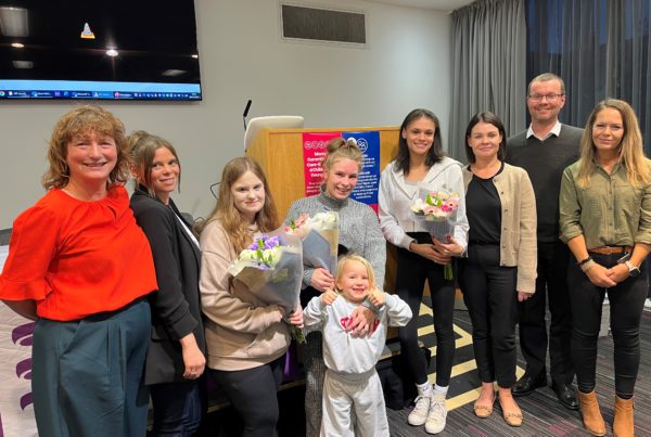 A group of adults and young adults, some holding bouquets of flowers, line up in front of a small stage in a conference room to mark the launch of the Maintaining relationships project.