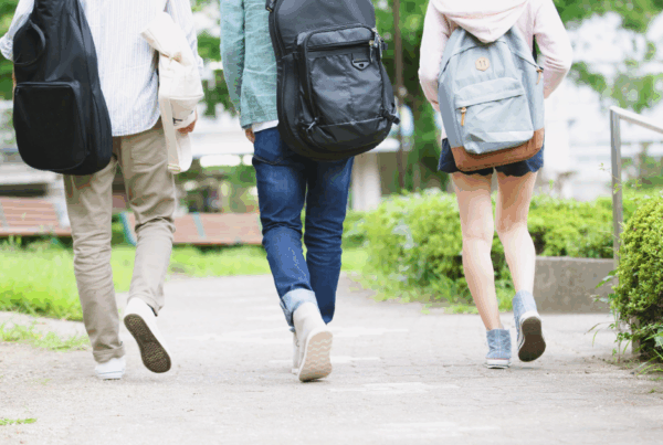 Three casually dressed young people walk away from the camera. One is carrying a rucksack on her back, the other two have guitars in soft carry cases.