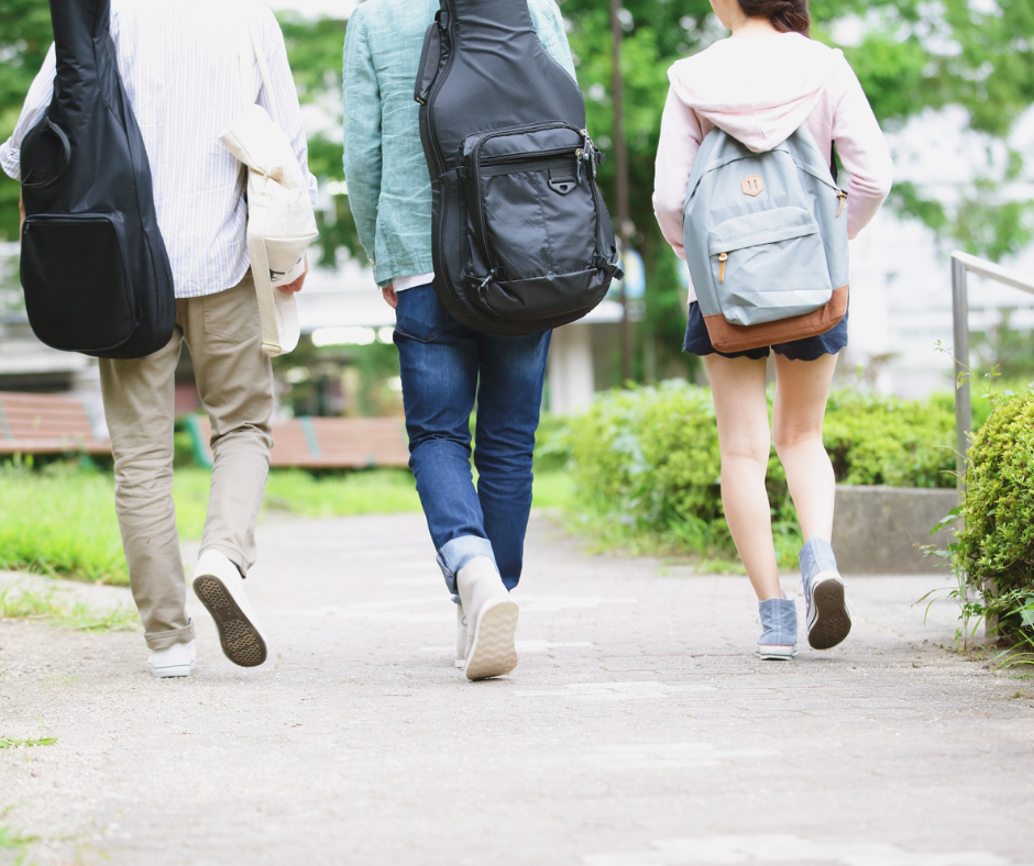 Three casually dressed young people walk away from the camera. One is carrying a rucksack on her back, the other two have guitars in soft carry cases.