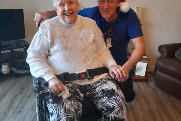 A wheelchair user sits in their home, with a social care assistant kneeling next to her.