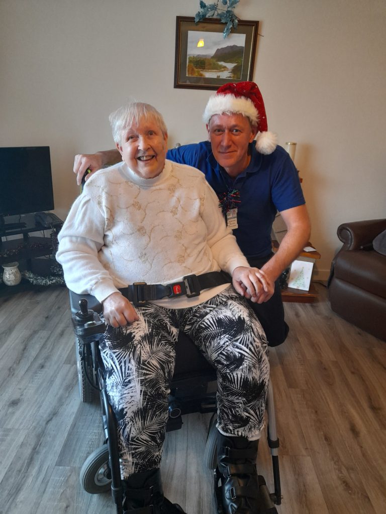 A wheelchair user sits in their home, with a social care assistant kneeling next to her.