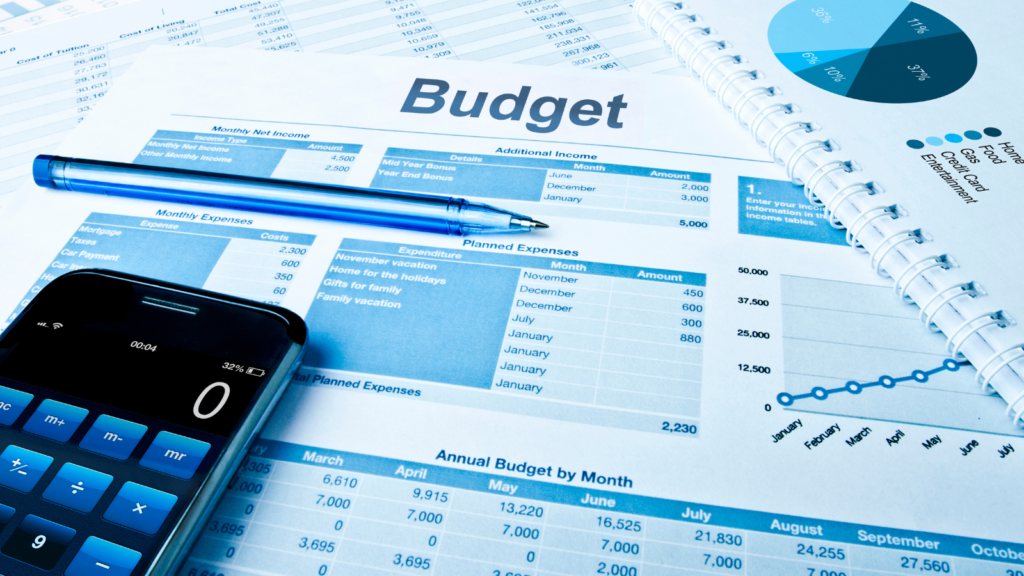A budget planning spreadsheet showing monthly income, expenses, and planned expenditures, alongside a calculator, pen, pie chart, and line graph, all in a blue colour scheme.