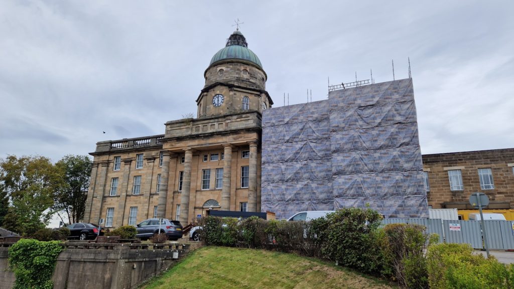 Front view of the Dr Gray's Hospital building In Elgin, showing the iconic sandstone walls, clocktower. Part of the right hand side of the building is obscured by scaffolding.