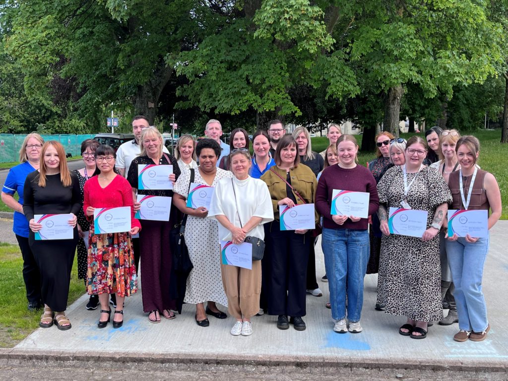 A group of staff members in an outdoor setting, holding certificates after an awards ceremony.