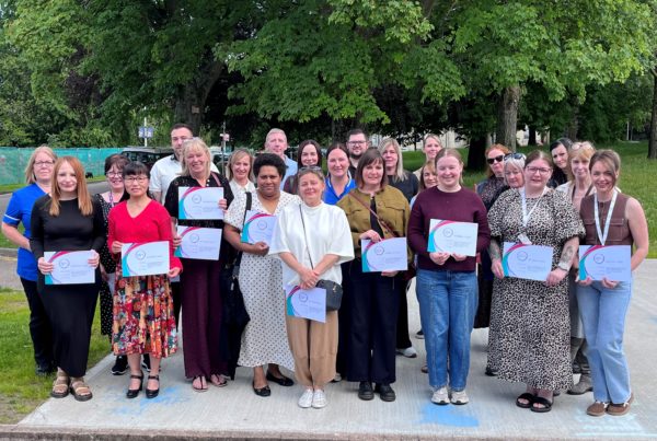 A group of staff members in an outdoor setting, holding certificates after an awards ceremony.