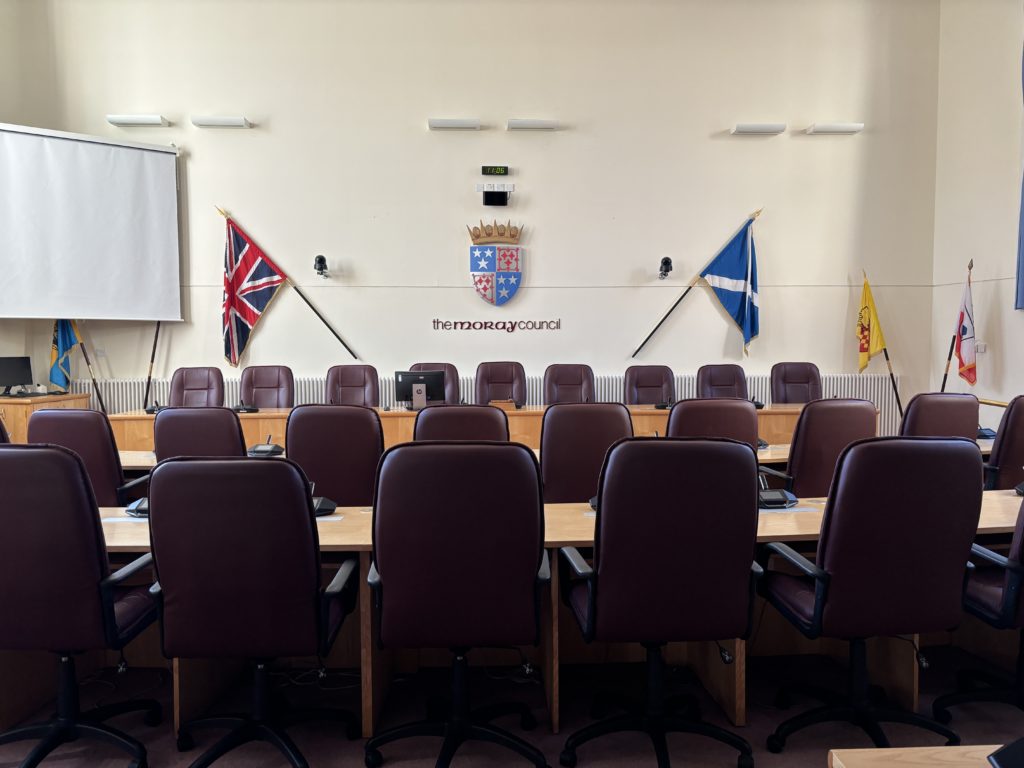 An interior view of the Moray Council chambers, taken rom the back to show the rows of seats with the raised top table.