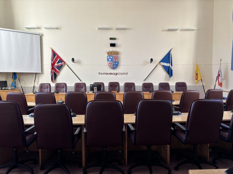 An interior view of the Moray Council chambers, taken rom the back to show the rows of seats with the raised top table.